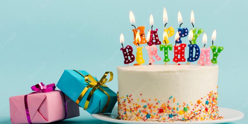 two-gift-boxes-near-cake-with-happy-birthday-candles-against-blue-backdrop_23-2148190488